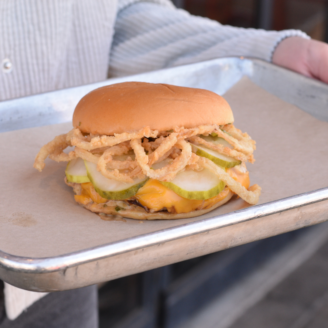 A sandwich with onions, pickles, cheese, and chicken on a tray being held
