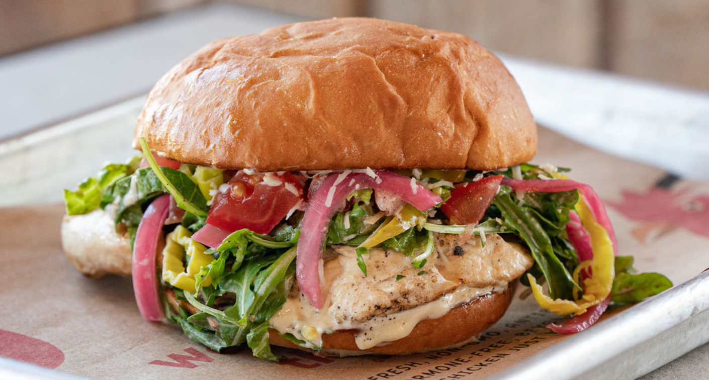 Image of a grilled chicken sandwich with greens on a tray.