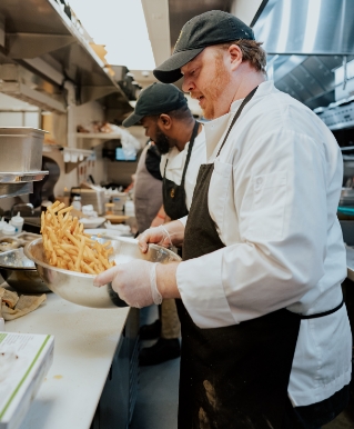 Image of a man tossing fresh french fries in a kitchen